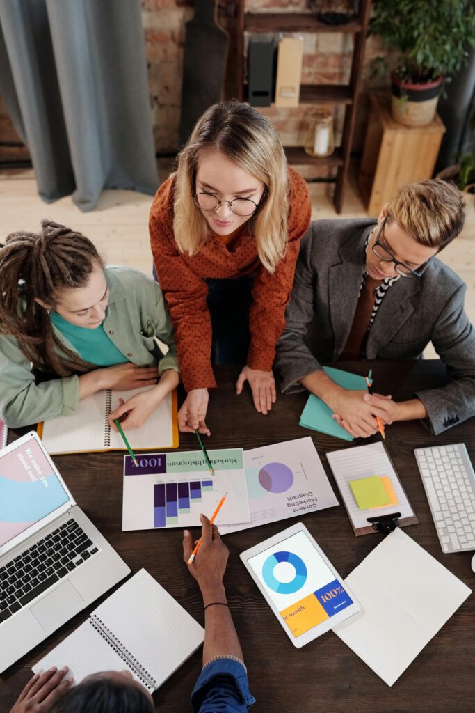 pexels-photo-6476245-6476245 Top view of a diverse group discussing business reports and charts around a desk.